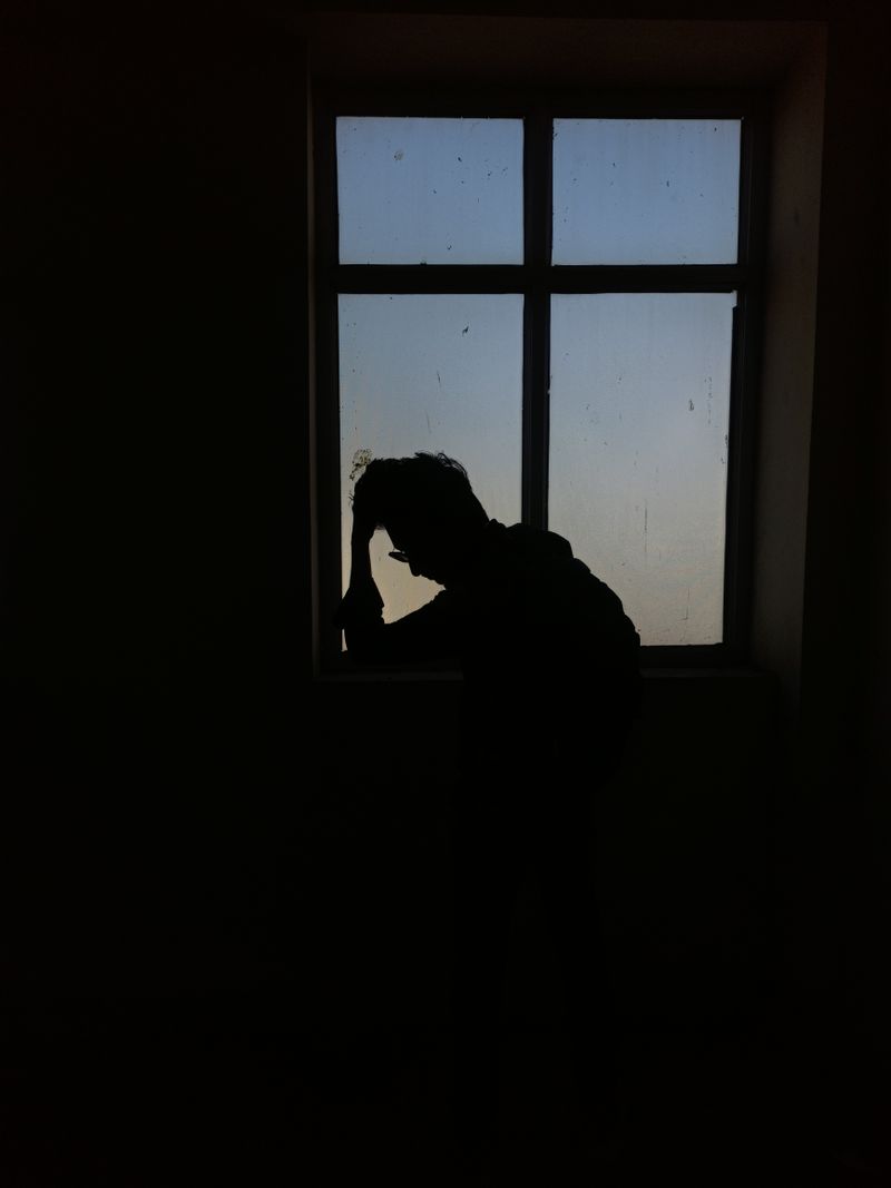 Silhouette of a person standing alone beside a window