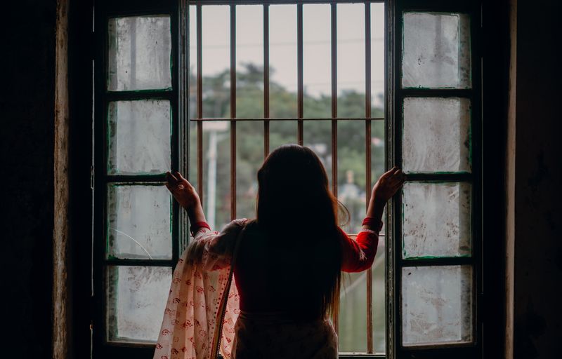 Silhouette of a woman looking out through a barred window