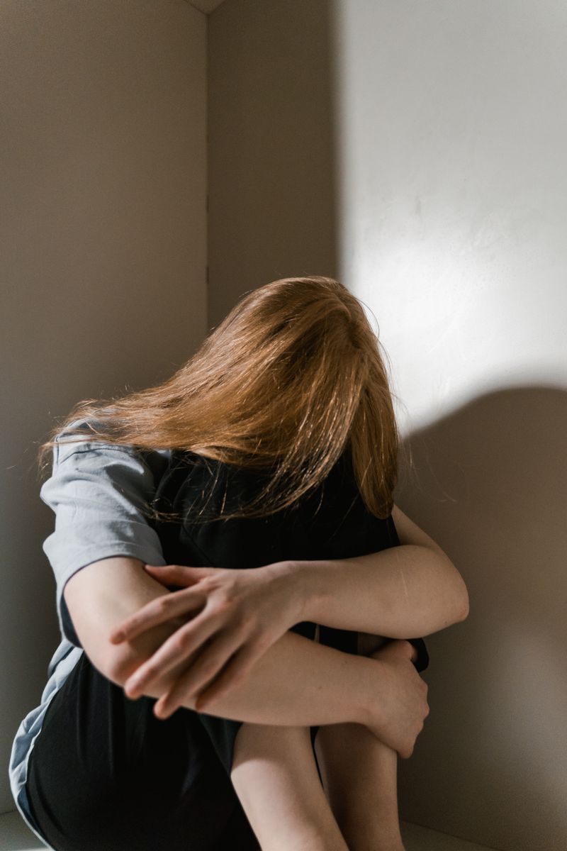 A woman sitting alone in a corner, head resting on her hand
